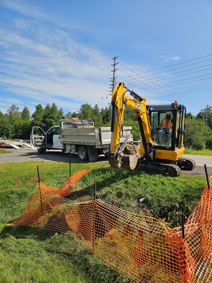 Excavator reinstating a roadside ditch behind safety fencing